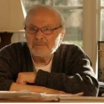 Maurice Sendak sitting at desk arms folded dark sweater glasses