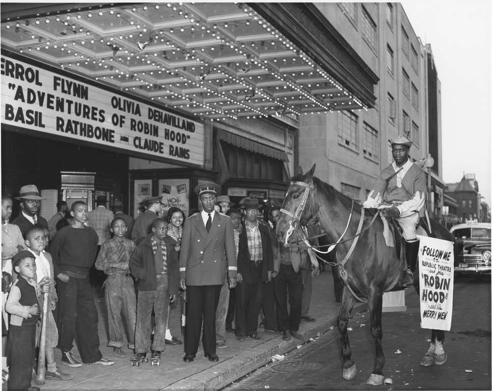 Kids and adults standing in front of DC theater in 1940. Man on horse promoting Robin Hood