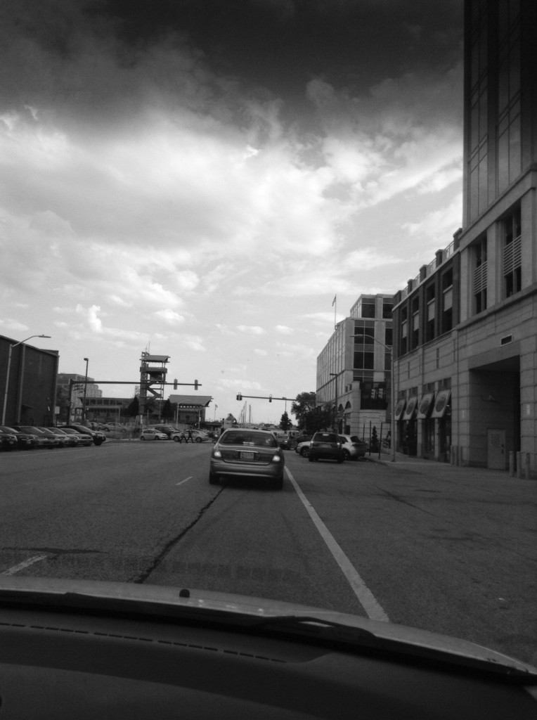 Black and white photo from a car showing clouds and cars