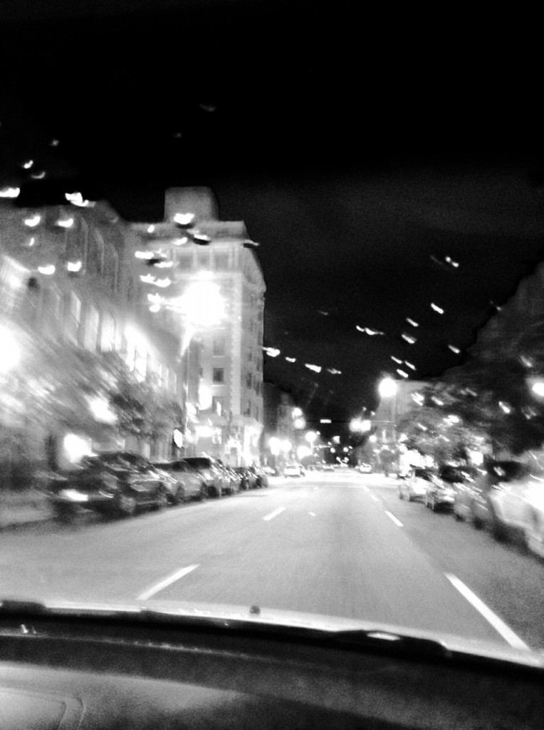 Blurry black and white photo of  a street at night taken from a car